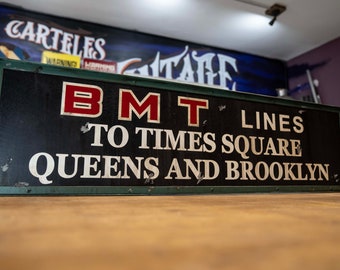 May include: A vintage black and green sign with white lettering that reads "BMT LINES TO TIMES SQUARE QUEENS AND BROOKLYN". The letters "BMT" are in red.