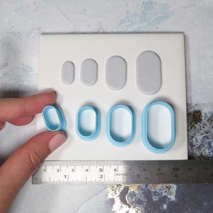 Könnte beinhalten: Ein Satz oval geformter Polymer Clay Ausstecher und passende Tonstücke in verschiedenen Größen. Die Ausstecher sind hellblau und die Tonstücke grau. Ein Lineal zeigt die Maße in Zentimetern an.