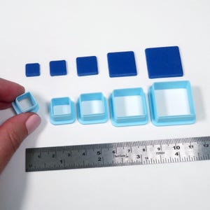 May include: A collection of blue square-shaped polymer clay cutters and solid squares in various sizes. A ruler is included for scale, showing measurements up to 12 inches. The cutters have a light blue frame with a white interior.