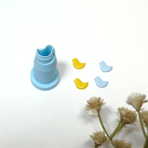 May include: A light blue plastic mould shaped like a bird, with four small bird-shaped pieces, two yellow and two light blue, on a white surface.