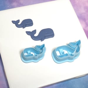 Op de afbeelding: Vier walvormige koekjessnijders. Twee zijn effen blauw en twee lichtblauw met een walvisomtrek. De uitstekers zijn gerangschikt op een wit oppervlak. De walvisvormen zijn voor bakken of knutselen.