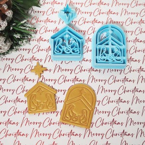 May include: Three cookie cutters in the shape of a nativity scene. The cutters are made of blue and gold plastic. The cutters are on a white background with the words "Merry Christmas" repeated.