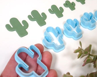 May include: A set of nine cactus-shaped cookie cutters in various sizes. The cutters are made of blue and green plastic. The cutters are arranged in a row on a white surface.