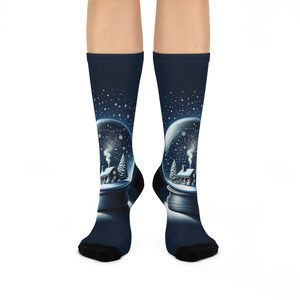 May include: A pair of navy blue socks featuring a snow globe design. The snow globe shows a winter scene with a house, trees, and falling snow. The socks have black heels and toes.