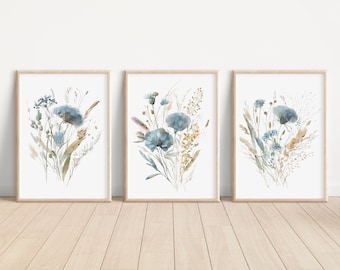 May include: Three framed watercolour prints featuring blue and brown wildflowers with a white background. The prints are arranged in a row on a light wood floor.