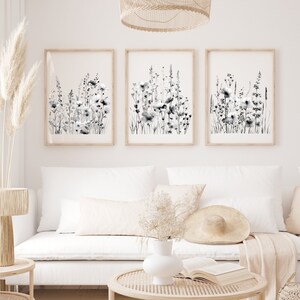 May include: Three black and white framed prints of watercolor floral illustrations. The prints are hung on a white wall above a white couch with a throw blanket and pillows.