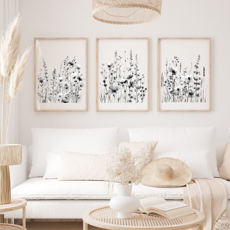 May include: Three black and white framed prints of watercolor floral illustrations. The prints are hung on a white wall above a white couch with a throw blanket and pillows.