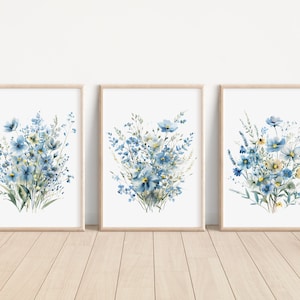 May include: Set of three watercolor prints featuring blue and yellow wildflowers in a minimalist style. The prints are framed in natural wood frames and are perfect for adding a touch of nature to any room.