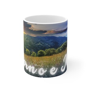 Può includere: Tazza in ceramica bianca con un'immagine panoramica di una catena montuosa al tramonto. Il testo "Born to e" è stampato sul fondo della tazza.