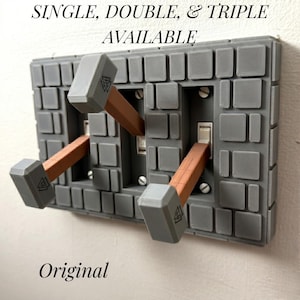 May include: A gray, brick-patterned double light switch cover plate featuring three hammer-shaped toggle extensions with brown handles and gray heads. The text "SINGLE, DOUBLE, & TRIPLE AVAILABLE" and "Original" is printed above and below the plate.