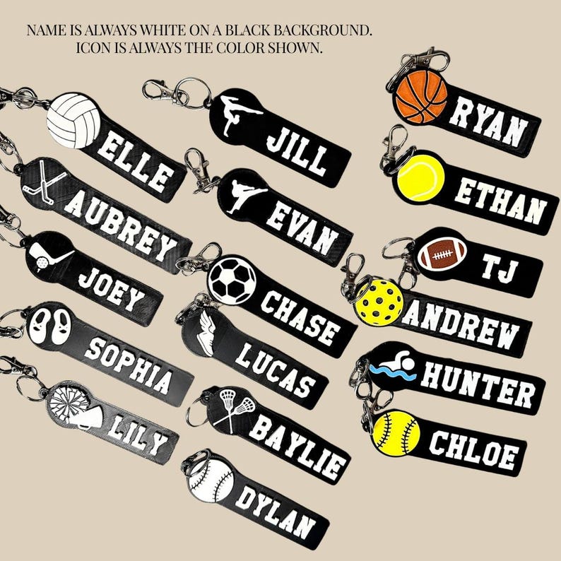 May include: A collection of rectangular black keychains featuring white personalized names and various sports icons including a volleyball, basketball, football, soccer ball, and tennis ball, each attached to a silver metal lobster claw clasp.