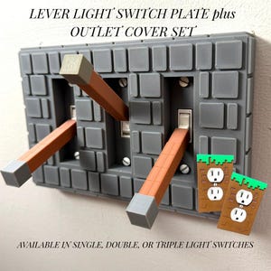 May include: Gray lever light switch plate and outlet cover set. The light switches have brown levers with gray tips. The outlet covers are brown with green tops. Text on the image reads "LEVER LIGHT SWITCH PLATE plus OUTLET COVER SET" and "AVAILABLE IN SINGLE, DOUBLE, OR TRIPLE LIGHT SWITCHES."
