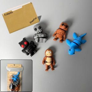 May include: A collection of five small, articulated monster figurines including a gray Cthulhu, a black Mothman with red eyes, a brown Bigfoot, a brown bear-like creature, and a blue Loch Ness monster, accompanied by a tan Evidence folder.