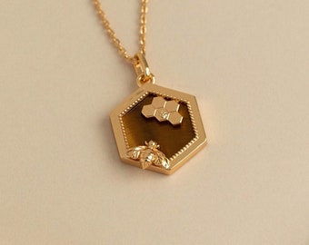 May include: A gold necklace with a hexagonal pendant featuring a bee and honeycomb design. The pendant has a brown, textured center.