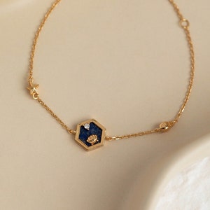 May include: A gold chain bracelet with a hexagonal charm featuring a blue stone and a small gold star.