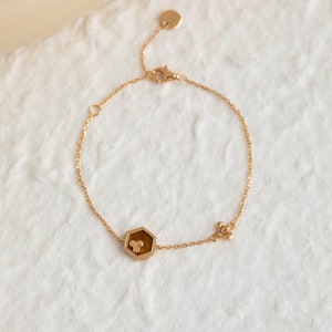 May include: A gold chain bracelet with a hexagonal charm featuring a honeycomb design and a small bee charm.