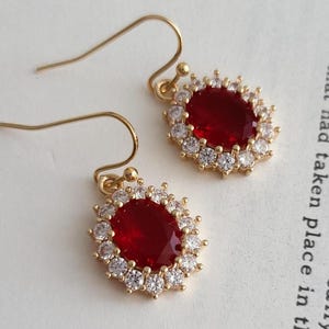 Peut inclure: Une paire de boucles d'oreilles en or avec des pierres précieuses ovales rouges entourées de petites pierres précieuses claires.