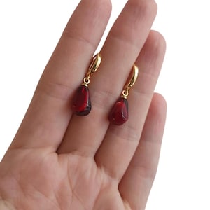 May include: A pair of gold hoop earrings with a dangling red teardrop-shaped gemstone.