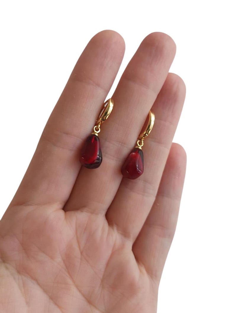 May include: A pair of gold hoop earrings with a dangling red teardrop-shaped gemstone.