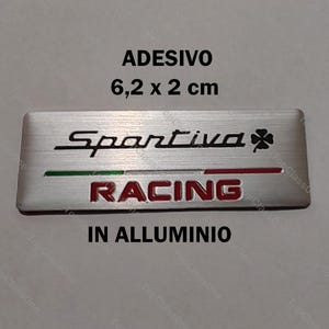 Può includere: Un adesivo Sportiva Racing rettangolare in alluminio, di circa 6,2 x 2 cm. L'adesivo presenta il logo Sportiva, un quadrifoglio e la scritta "RACING" in rosso. È presente anche la scritta "IN ALLUMINIO".