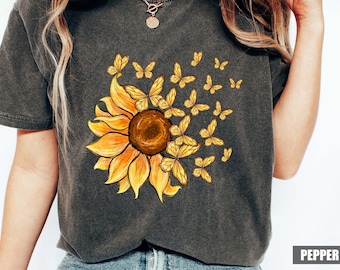 May include: A dark grey t-shirt with a yellow sunflower and butterflies printed on the front. The sunflower has a brown centre and yellow petals. The butterflies are yellow and flying away from the sunflower.