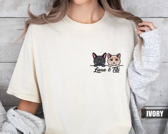 May include: A woman wearing a white t-shirt with a black and white cat illustration and the text "Luna & Tili" printed on the front. The shirt is ivory in color.
