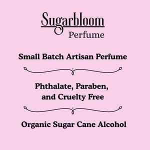 May include: A pink background with the text "Sugarbloom Perfume" in a decorative font. Below, it reads "Small Batch Artisan Perfume," followed by "Phthalate, Paraben, and Cruelty Free," and "Organic Sugar Cane Alcohol."