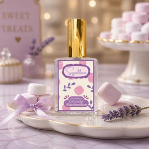 May include: A perfume bottle with a gold cap and a label that reads "Lavender Marshmallow." The label has a light purple background with pink marshmallow illustrations. The bottle sits on a white plate with marshmallows and a lavender sprig.