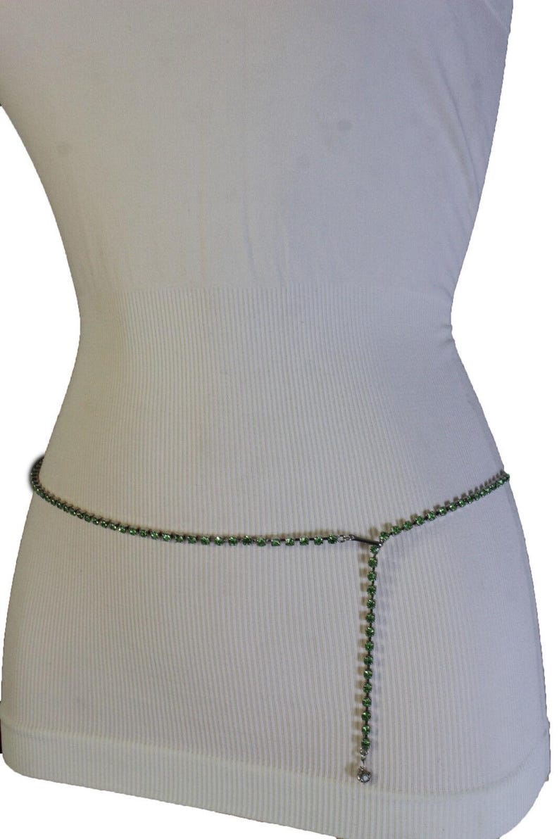 K&ouml;nnte beinhalten: Eine zarte gr&uuml;ne Strass-Taillenkette. Die Kette wird auf einer wei&szlig;en Schaufensterpuppe pr&auml;sentiert, um ihr Design zu zeigen. Sie besteht aus kleinen, runden gr&uuml;nen Strasssteinen, die durch d&uuml;nnes, silberfarbenes Metall verbunden sind.