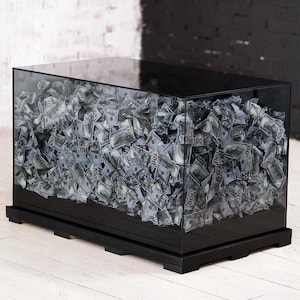 May include: A black glass box filled with fake $100 bills, sitting on a black wooden base. The box is on a white wooden floor.