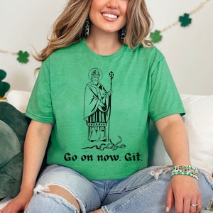 May include: A green t-shirt with a black and white illustration of a saint holding a staff. The text "Go on now. Git." is printed below the illustration.