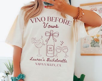 Puede incluir: Camiseta color crema con un gráfico burdeos. El gráfico incluye el texto "Vino Before Vows" y "Lauren's Bachelorette, Napa Valley, CA", junto con ilustraciones de una botella de vino, copas y una persona relajándose en una copa.
