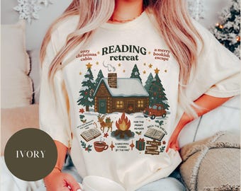 Puede incluir: Camiseta color marfil con un diseño de cabaña nevada, un coche y una fogata. El texto incluye "Reading Retreat", "Cozy Christmas Cabin" y "Christmas Stories by the Fire".