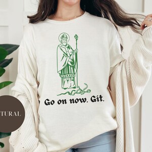 May include: A white sweatshirt with a green illustration of a man with a beard and a snake. The text "Go on now. Git." is printed below the illustration.