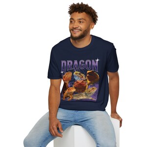 Puede incluir: Una camiseta azul marino con un gr&aacute;fico de varios dragones barbudos sobre un fondo morado. El texto "DRAGON" est&aacute; impreso en blanco con un contorno morado.