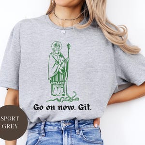 May include: A gray t-shirt with a green illustration of a man holding a staff. The text "Go on now. Git." is printed on the shirt.