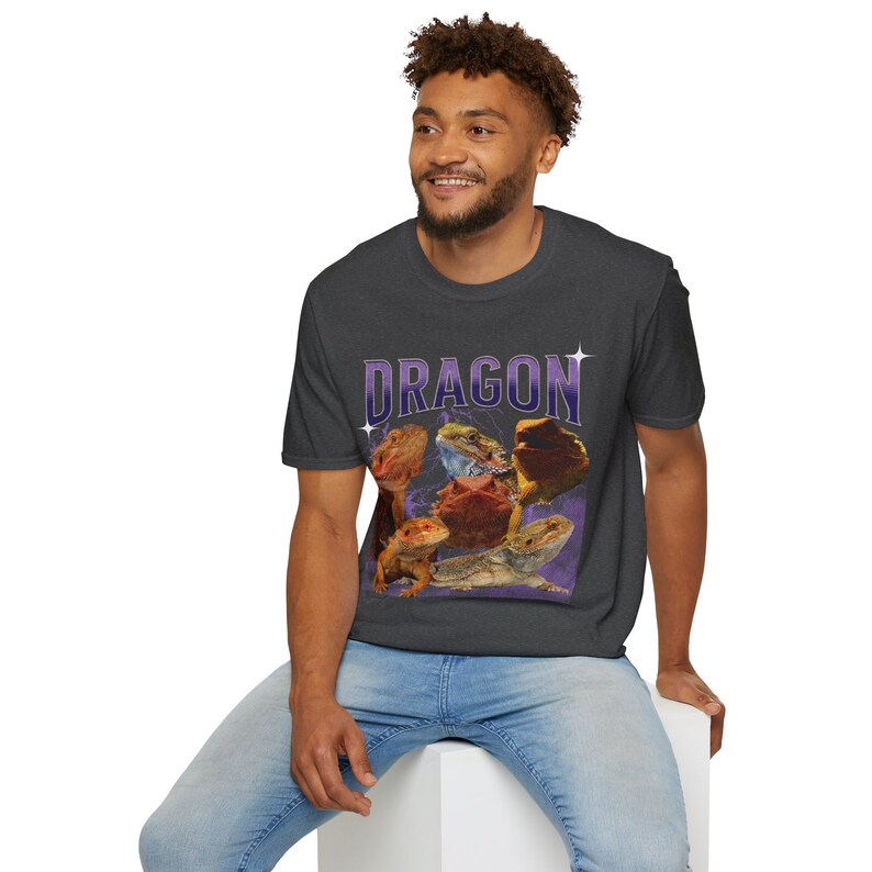 Puede incluir: Una camiseta gris oscuro con un gr&aacute;fico de varios dragones barbudos sobre un fondo morado. El texto "DRAGON" est&aacute; impreso en morado en la camiseta.