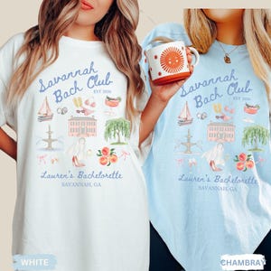 May include: Two t-shirts, one white and one light blue, featuring a watercolor design. The design includes a sailboat, sunglasses, a cocktail, and the text "Savannah Bach Club EST 2026" and "Lauren's Bachelorette, Savannah, GA."