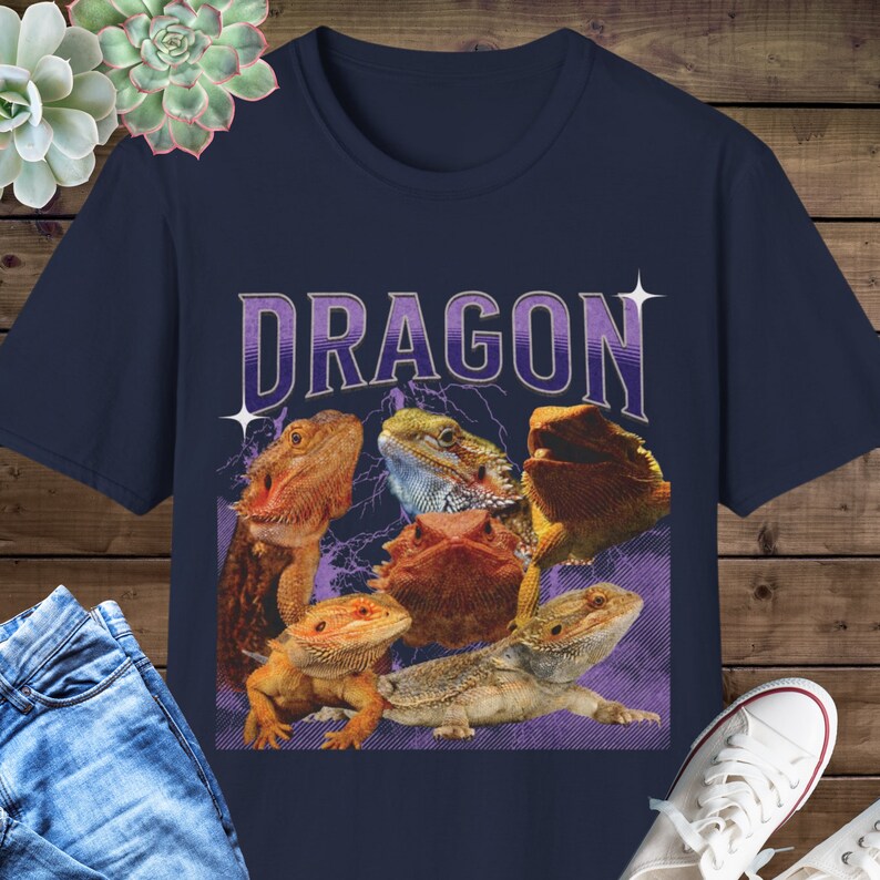 Puede incluir: Una camiseta azul marino con un gr&aacute;fico de cinco dragones barbudos. El texto "DRAGON" est&aacute; impreso en morado y blanco en la camiseta.