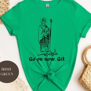 May include: A green t-shirt with a black illustration of a saint holding a staff. The text "Go on now. Git." is printed below the illustration.