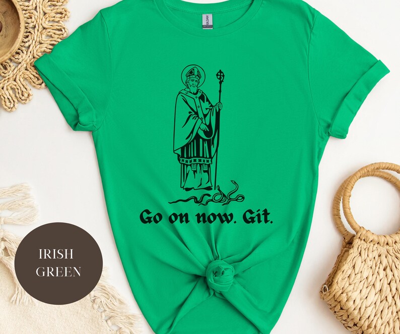 May include: A green t-shirt with a black illustration of a saint holding a staff. The text "Go on now. Git." is printed below the illustration.