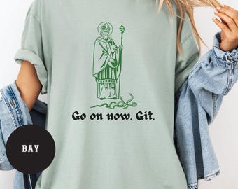 Puede incluir: Una camiseta verde claro con una ilustración verde de un hombre con una túnica sosteniendo un bastón. El texto "Go on now. Git." está impreso debajo de la ilustración.