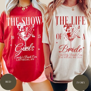 May include: Two t-shirts, one red and one ivory, with a graphic of a woman in a martini glass. The red shirt reads "THE SHOW Girls Emily's Bach Era LAS VEGAS, NV 2025". The ivory shirt reads "THE LIFE OF A Bride In My Bride Era LAS VEGAS, NV 2025".