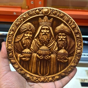 May include: A round wooden plaque with a detailed carving of the three wise men. The men are depicted in traditional robes and holding gifts. The plaque is surrounded by a decorative border.