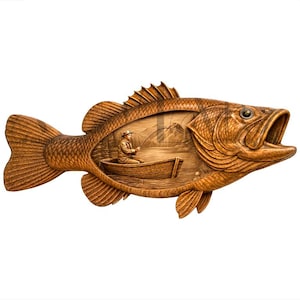 May include: A detailed wooden carving of a fish with an open mouth. Inside the fish is a carved scene of a person fishing from a boat. The carving is a warm brown color and has intricate details.