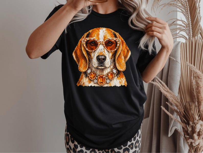 May include: A black short-sleeved t-shirt featuring a graphic print of a brown and white beagle dog wearing orange-tinted cat-eye glasses and a large, ornate necklace made of faceted orange and clear gemstones set in a metallic frame.