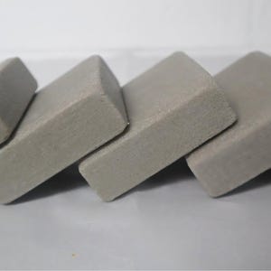 May include: A row of five gray erasers, each rectangular with beveled edges, arranged in a slightly angled line. The erasers are a uniform color and appear to be made of a soft, pliable material, suitable for removing pencil marks.