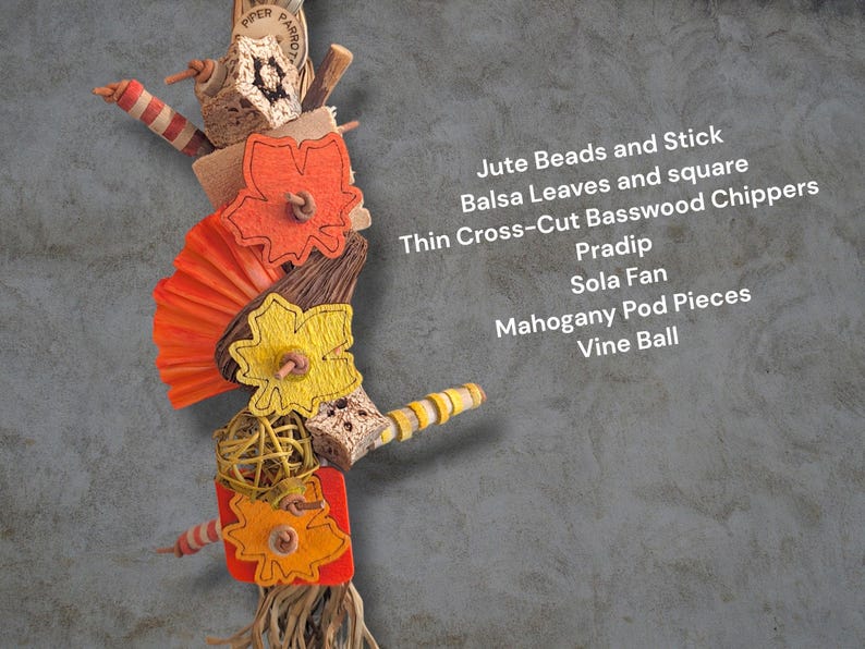 May include: A bird toy featuring orange and yellow felt leaves, a bright orange sola fan, a yellow vine ball, mahogany pod pieces, balsa wood squares, and basswood chippers. Text reads: Jute Beads and Stick, Balsa Leaves and square, Thin Cross-Cut Basswood Chippers, Pradip, Sola Fan, Mahogany Pod Pieces, Vine Ball.