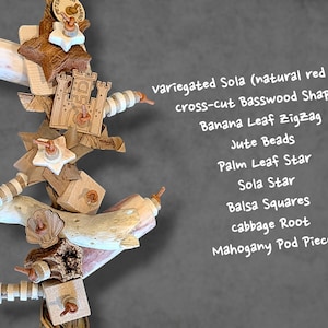 May include: A bird toy featuring variegated Sola with natural red hues, cross-cut Basswood shapes, a banana leaf zigzag, jute beads, a palm leaf star, a Sola star, balsa squares, cabbage root, and a mahogany pod piece, all strung together.