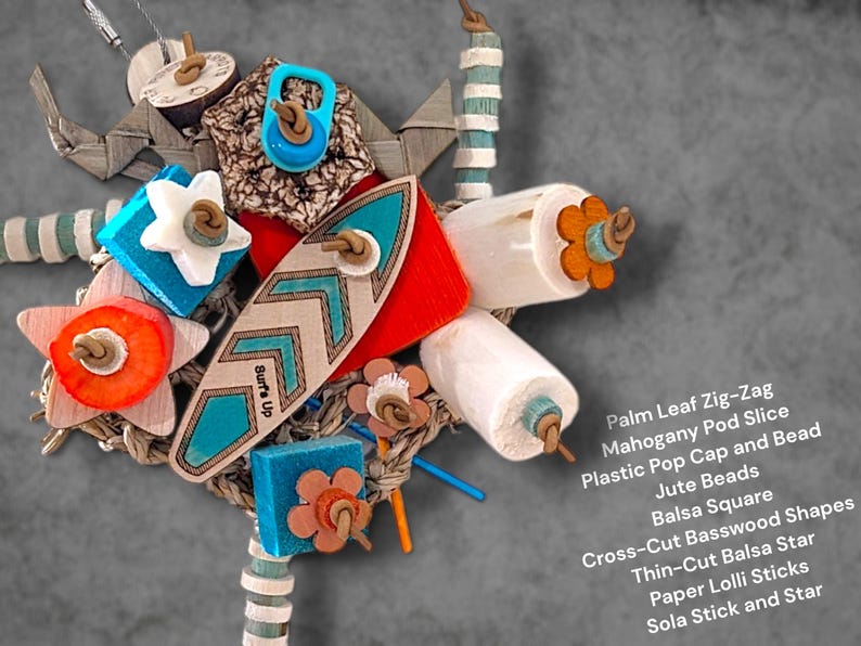 May include: A multi-textured bird toy featuring a central wooden surfboard shape with the text Surf's Up, surrounded by palm leaf zig-zags, mahogany pod slices, plastic pop caps, jute beads, balsa squares, cross-cut basswood, and sola sticks.